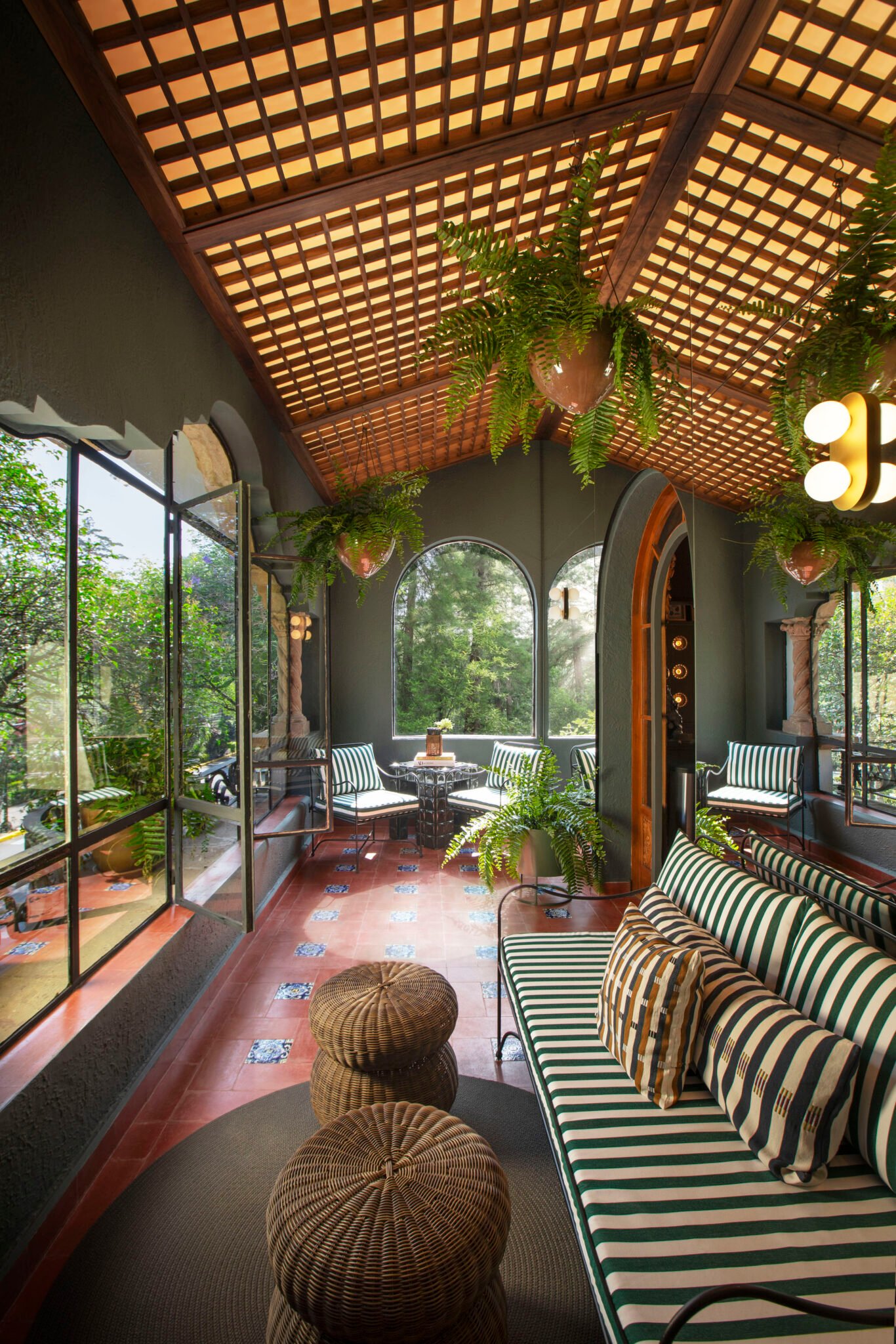 Galerie couverte avec plantes, banquette rayée et poufs tressés
