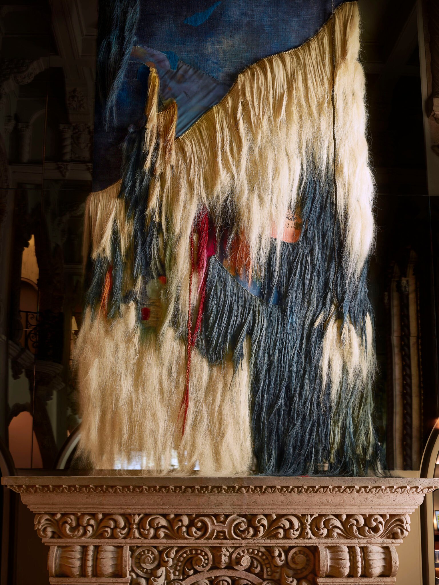 Œuvre textile monumentale aux fibres claires et bleues au-dessus d’une cheminée sculptée
