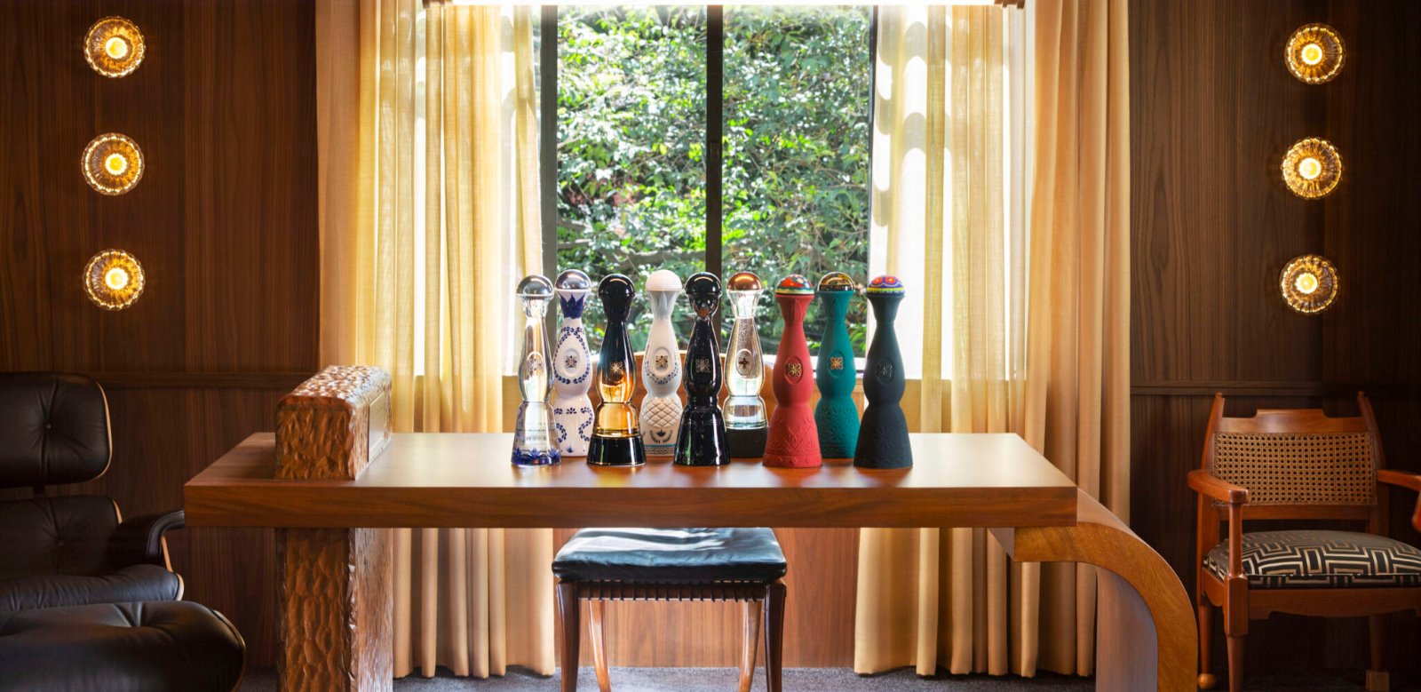 Salle aux boiseries avec table en bois et décanteurs Clase Azul alignés devant une fenêtre