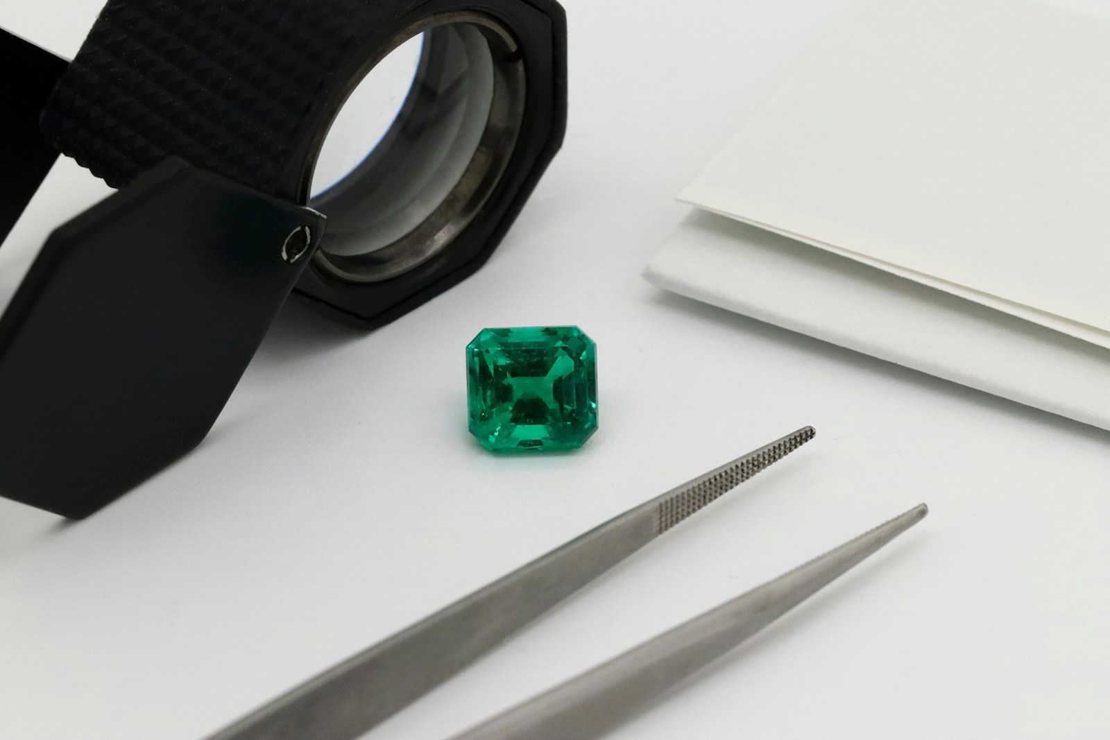 Émeraude taillée, loupe et pinces de gemmologue