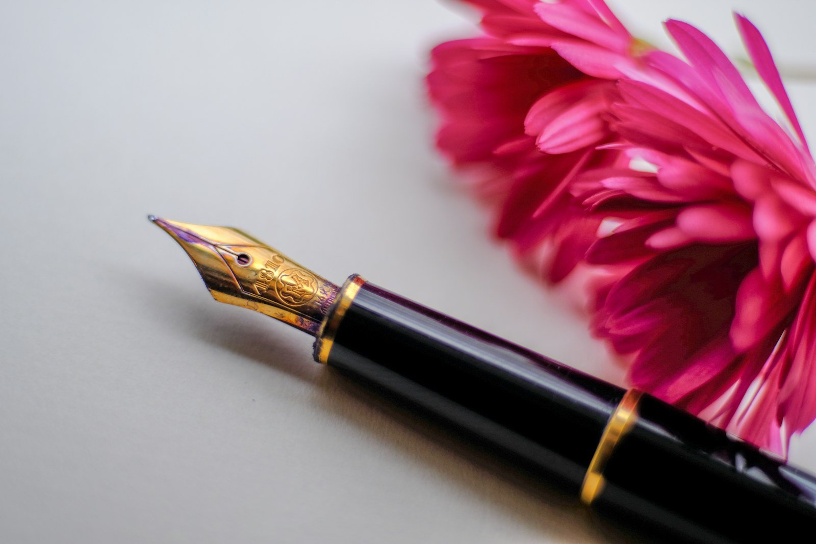 Stylo plume noir et or à côté d'une fleur rose, le pouvoir féminin selon Nadine de Rothschild