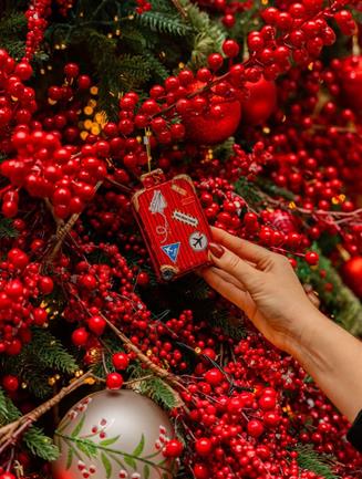 Main suspendant une boule de Noël dans des branches de baies rouges
